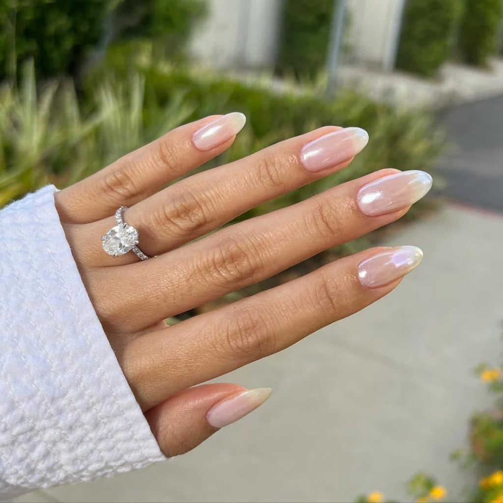 A woman's hand with pink ombre almond nails and a diamond engagement ring.