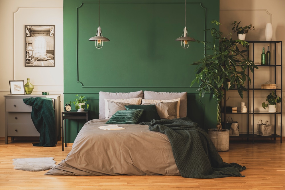 Modern bedroom with a green wall, wooden floors, pendant lights, and a large indoor plant.