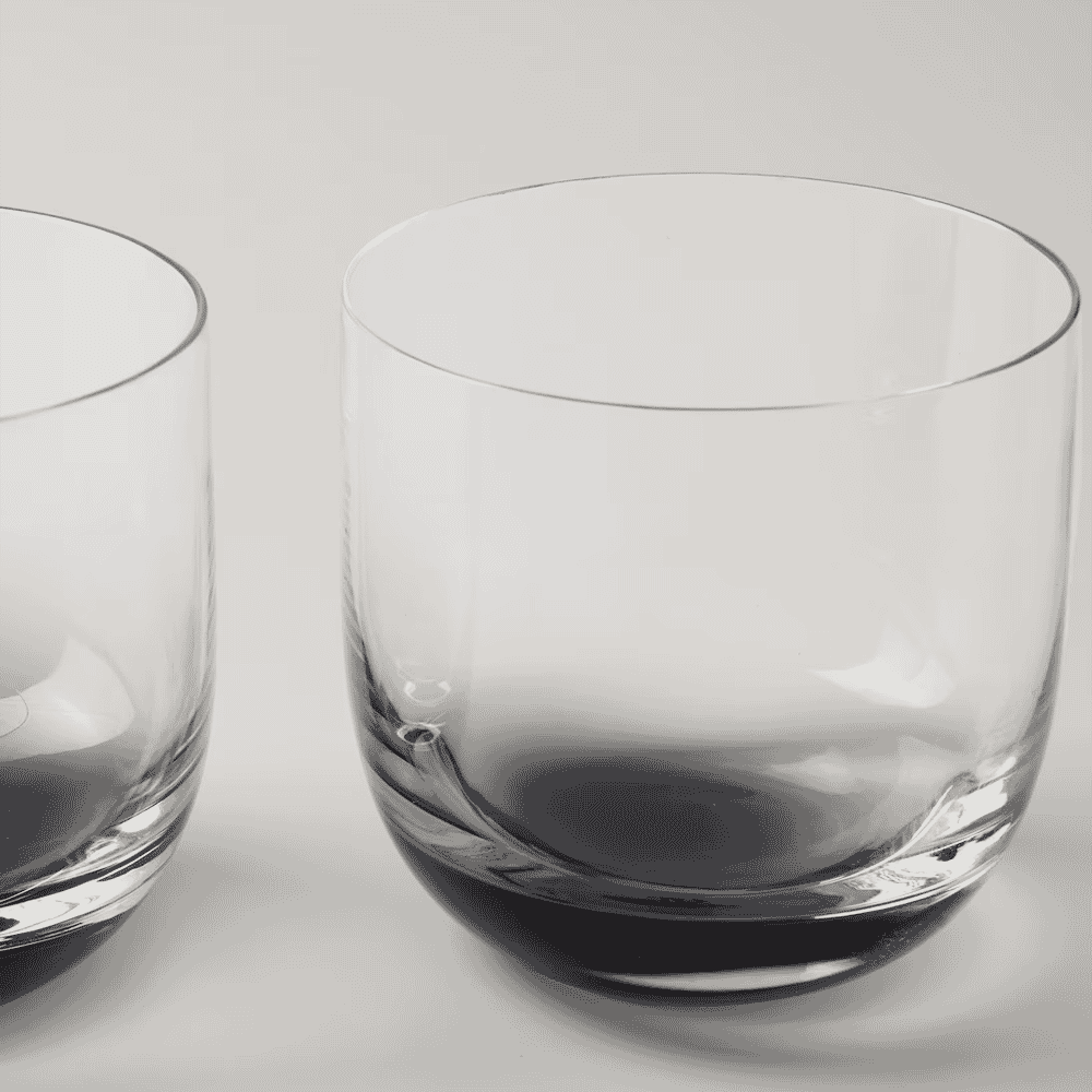 Two modern, clear glasses with rounded bases on a minimalist neutral surface.