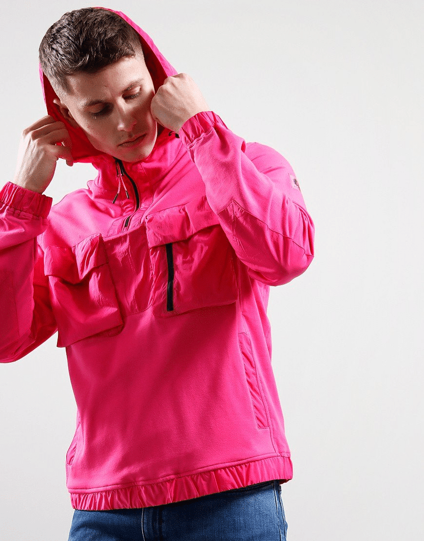 Man in a bright pink windbreaker adjusting his hood, symbolizing readiness for travel.
