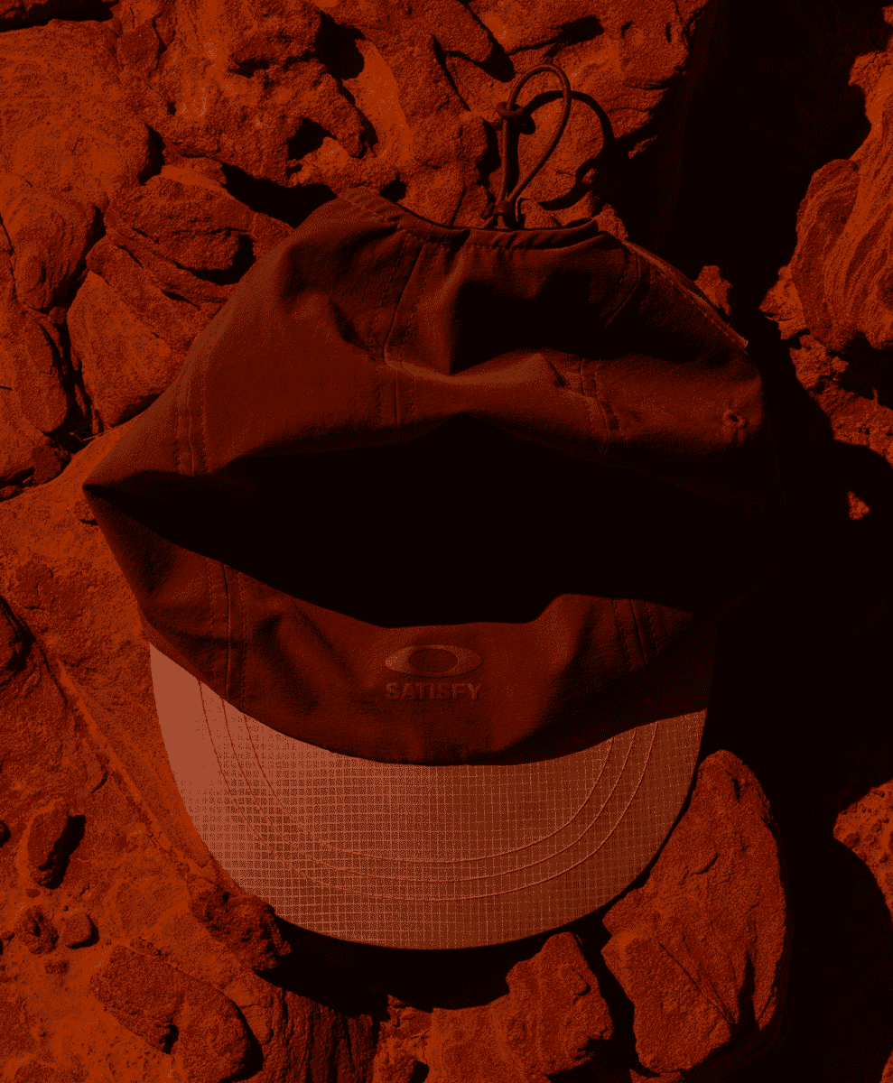 Brown Oakley Satisfy cap resting on reddish rocks under warm lighting.