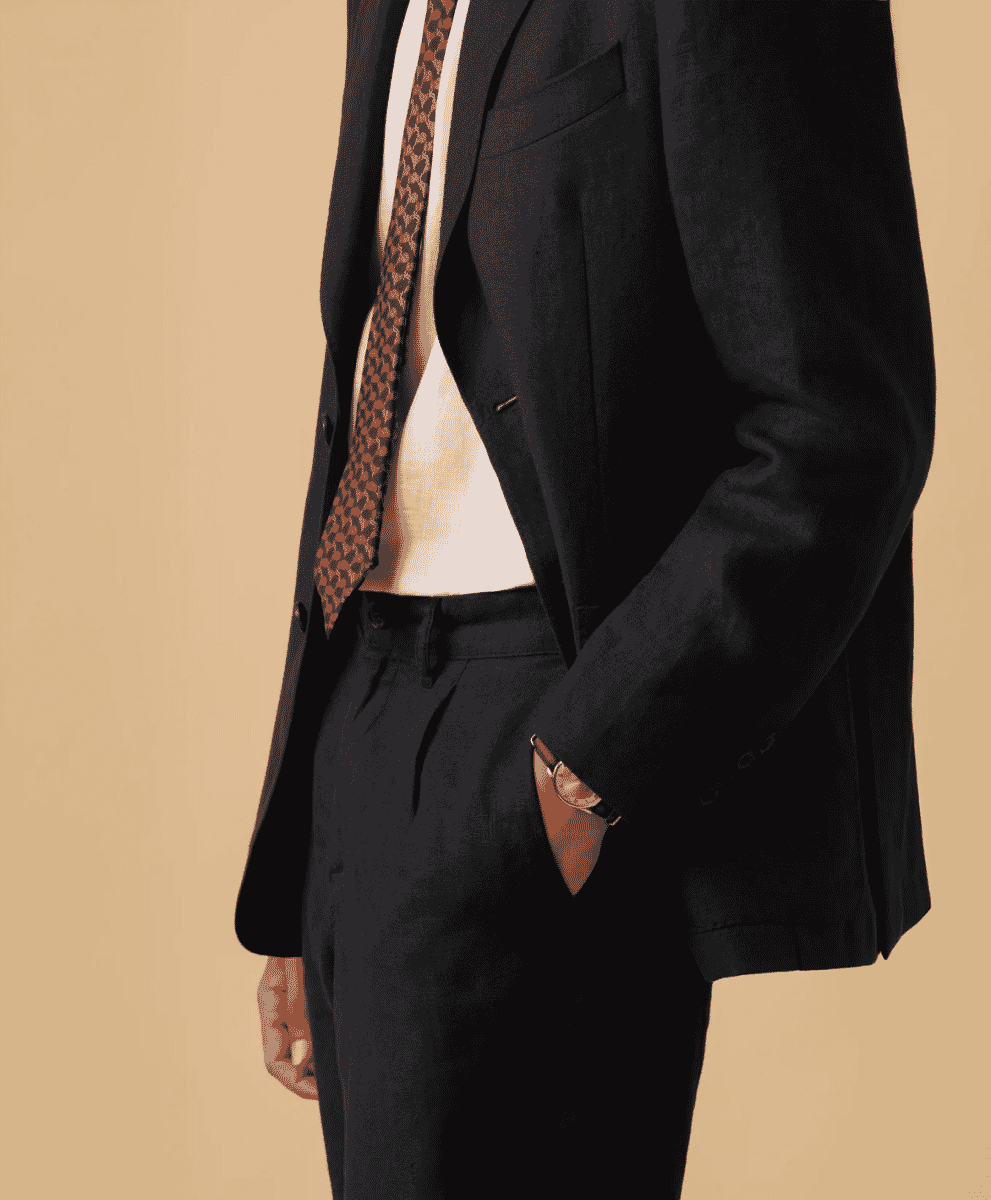 Close-up of a man in a dark tailored suit jacket with a patterned tie and cream shirt.