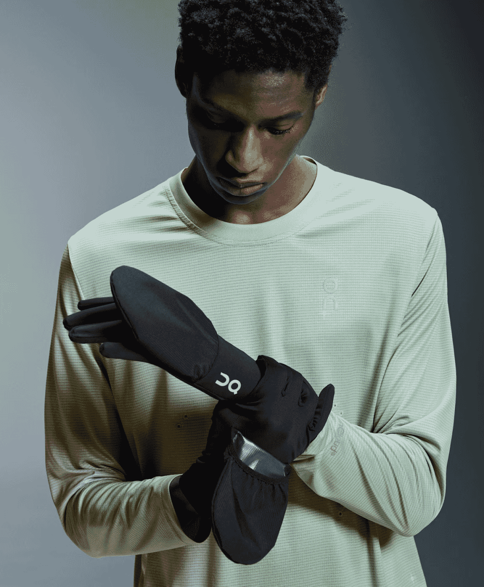 A person putting on black convertible athletic gloves with visible branding.