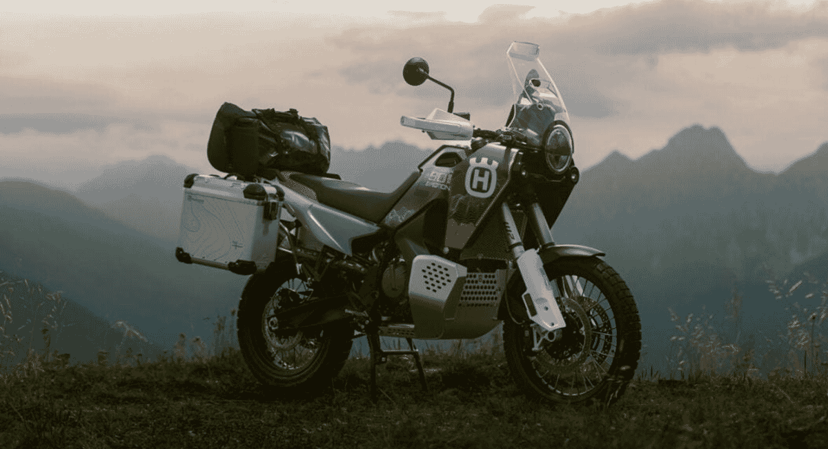 A parked adventure motorcycle with touring gear and luggage in a misty alpine setting.