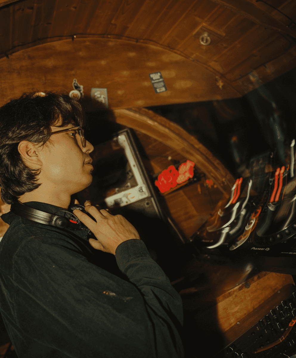 A DJ adjusting equipment in a warmly lit wooden booth.