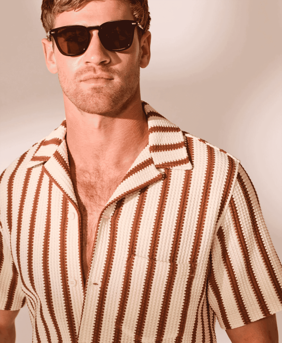 A man in a brown and cream striped knitted short-sleeve shirt with sunglasses.