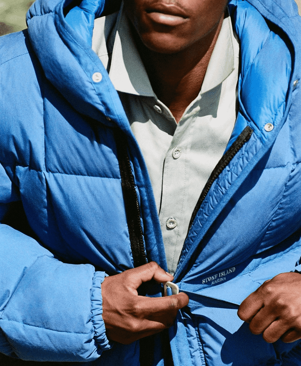 Close-up of a man zipping a blue puffer jacket with Stone Island Marina branding on the chest.