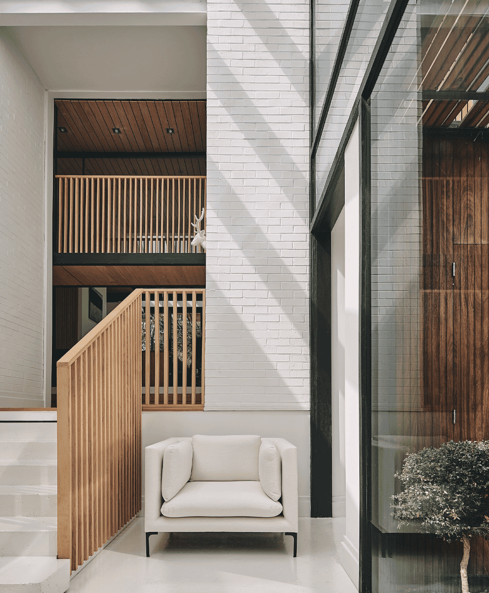 Minimalist white armchair against a white brick wall with architectural wooden accents.