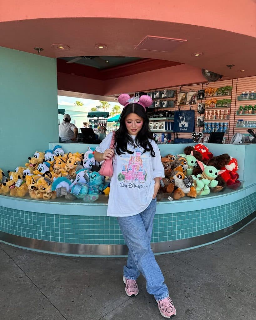 A woman in an oversized white Disney tee and baggy jeans posing near a merchandise kiosk.