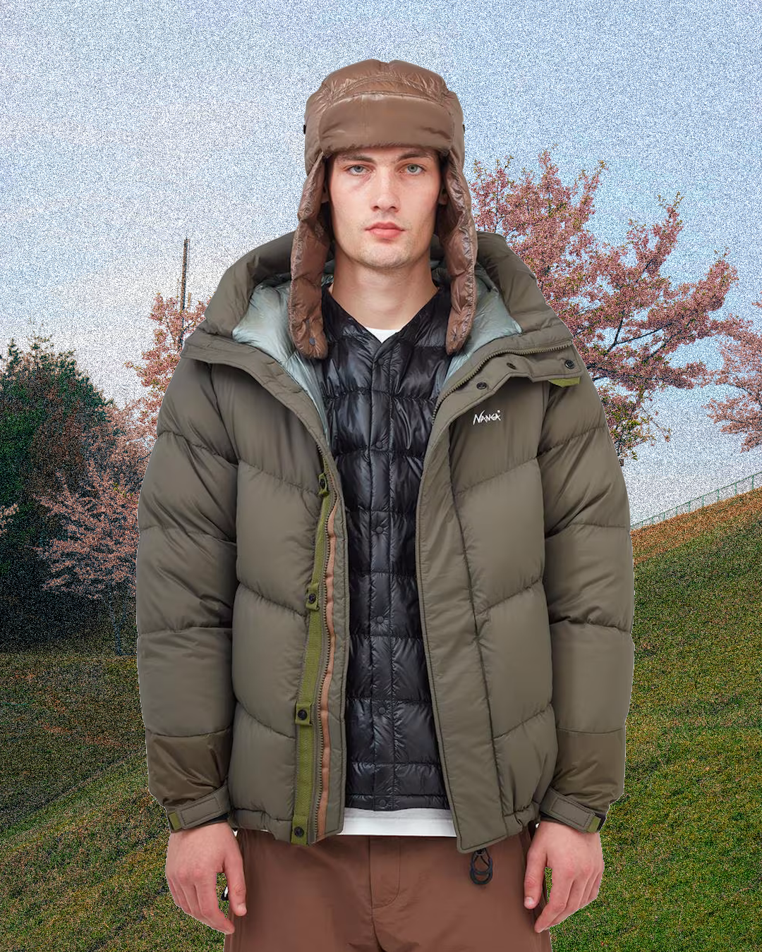Model wearing an olive green puffer, black quilted vest, and brown trapper hat.