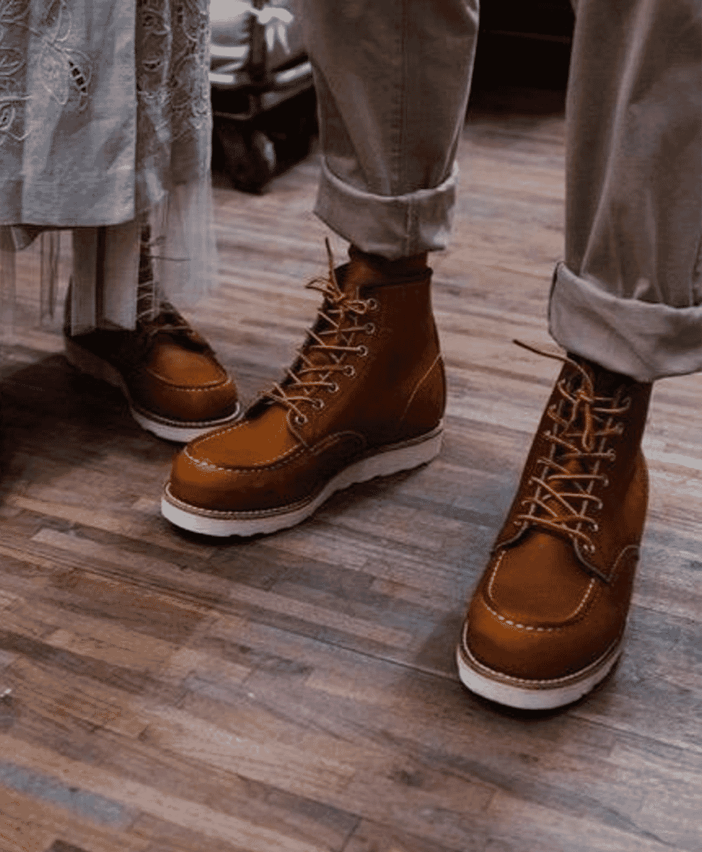 Two people wearing brown leather work boots with white soles and cuffed denim pants.