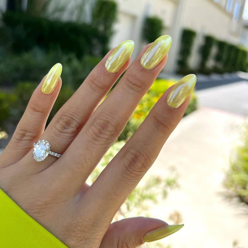 Glossy yellow nails with a diamond engagement ring against a sunny background.