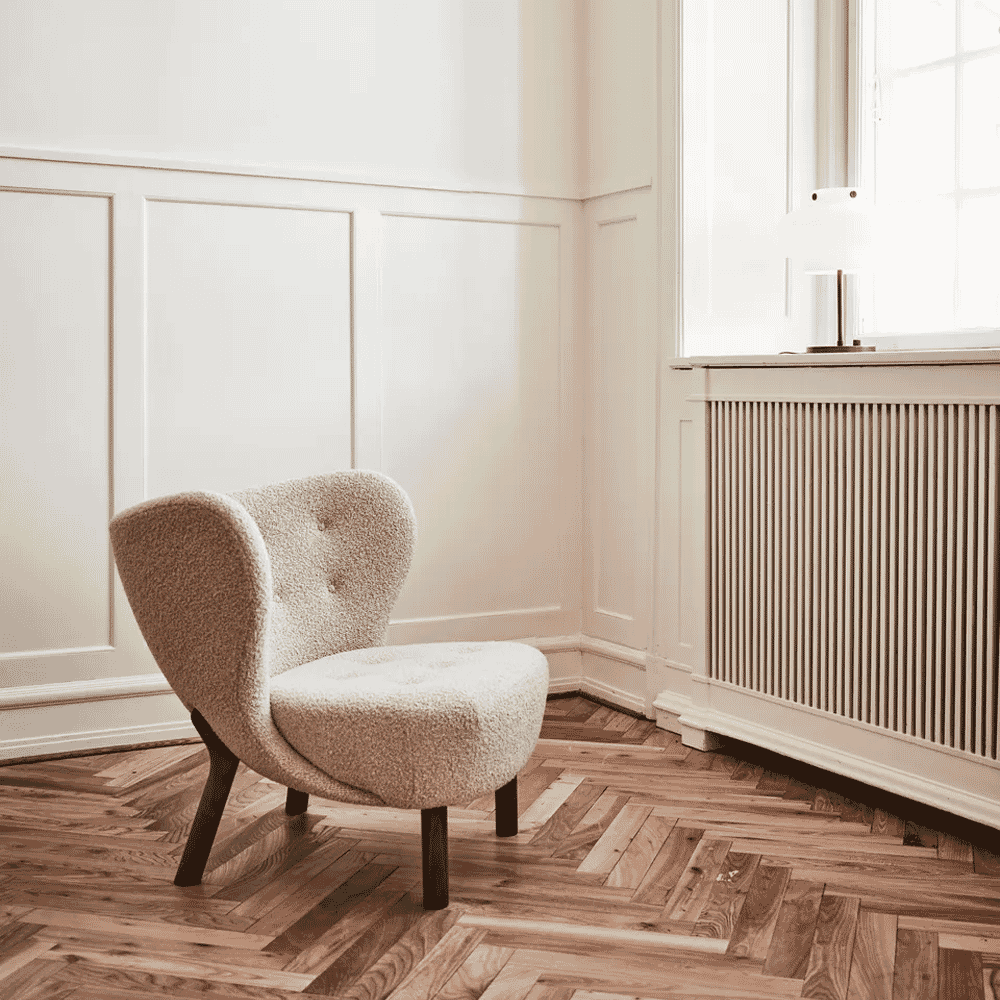 A cream-colored bouclé armchair on a herringbone wood floor in a bright room.