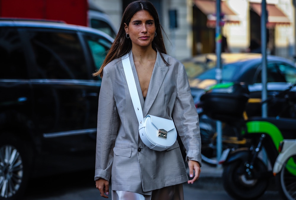 A street-style shot of a woman pairing a structured blazer with black leggings and chunky urban trainers.