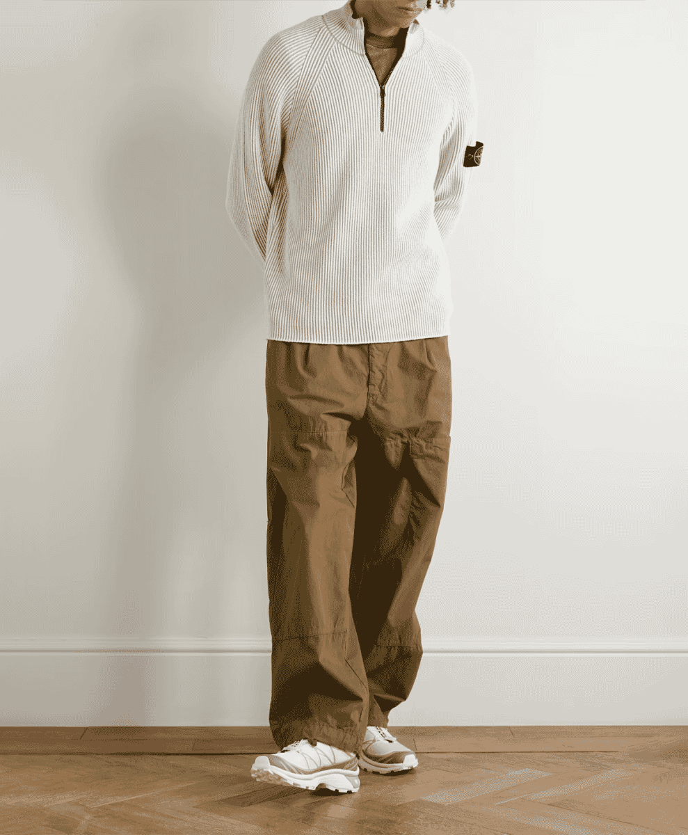 A model in a white Stone Island ribbed half-zip sweater paired with brown cargo pants.