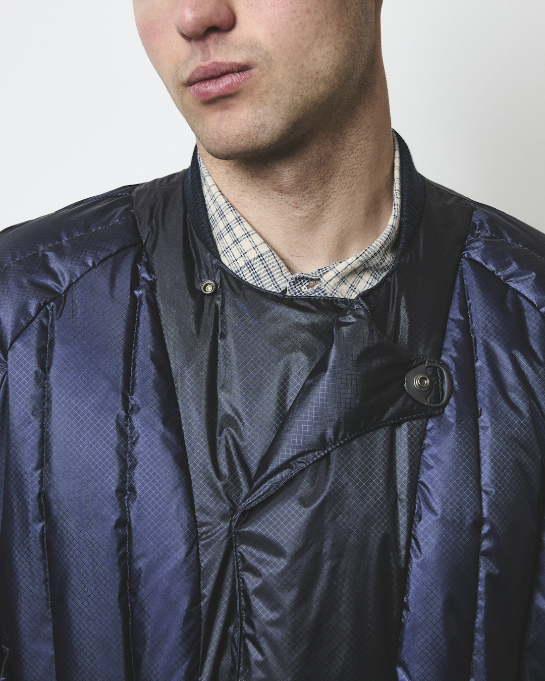 Close-up of a man wearing a dark blue quilted bomber jacket with a geometric pattern.