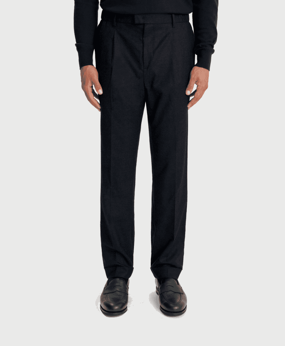 A man modeling black pleated trousers with a black sweater and leather loafers.