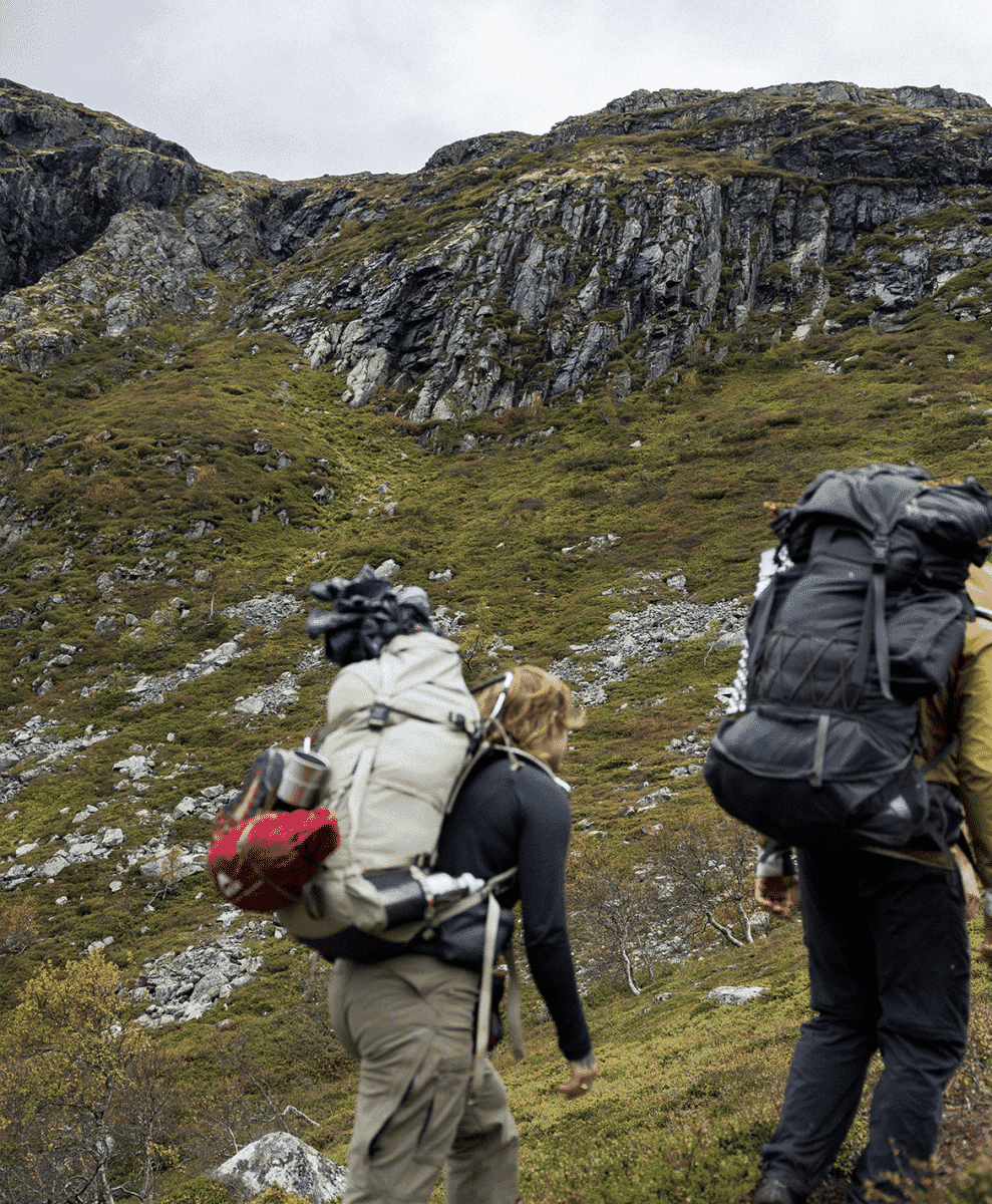 Hikers wearing technical backpacks and shells trekking across a steep, mossy mountain slope.