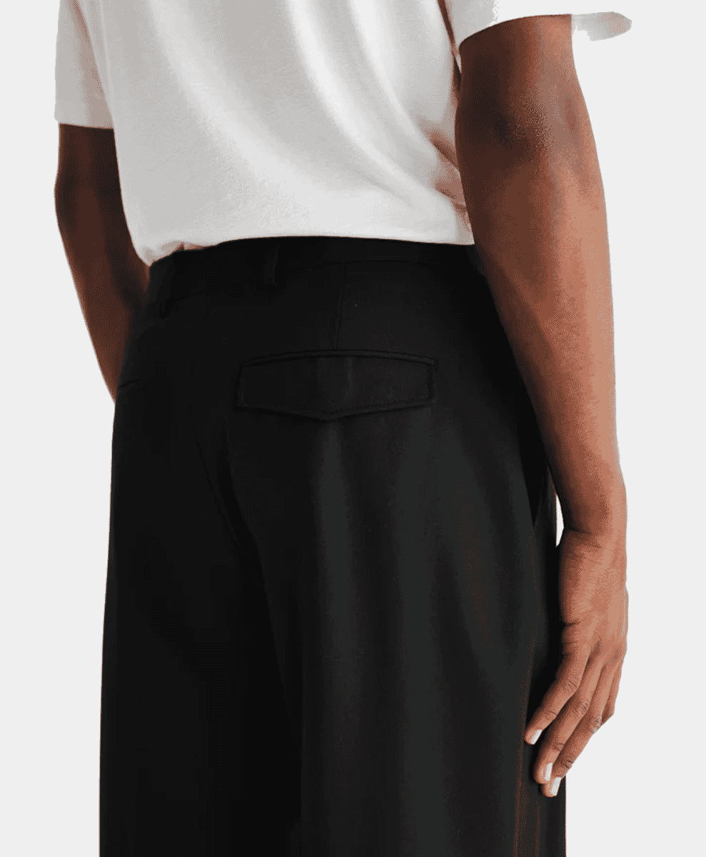 Detail view of black pleated trousers with a minimalist fit.