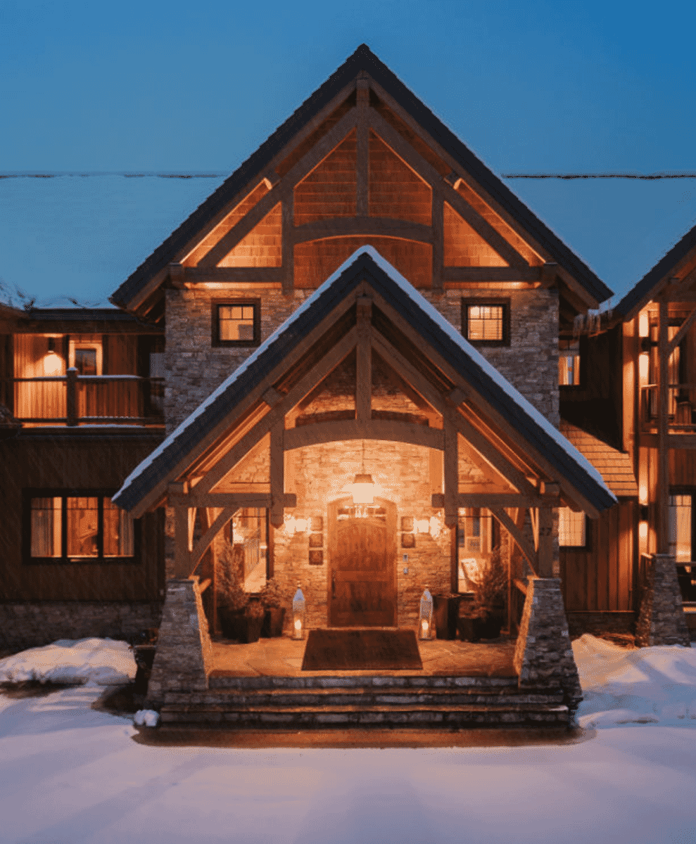 A snow-covered lodge made of stone and timber with warm yellow lights glowing inside at night.