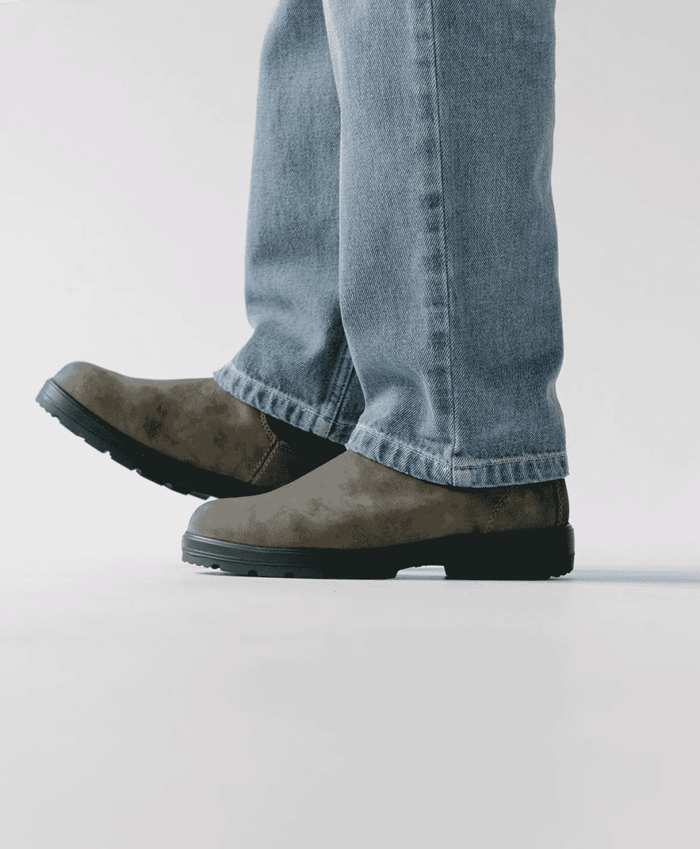 Person wearing brown suede boots with cuffed light-wash denim jeans.