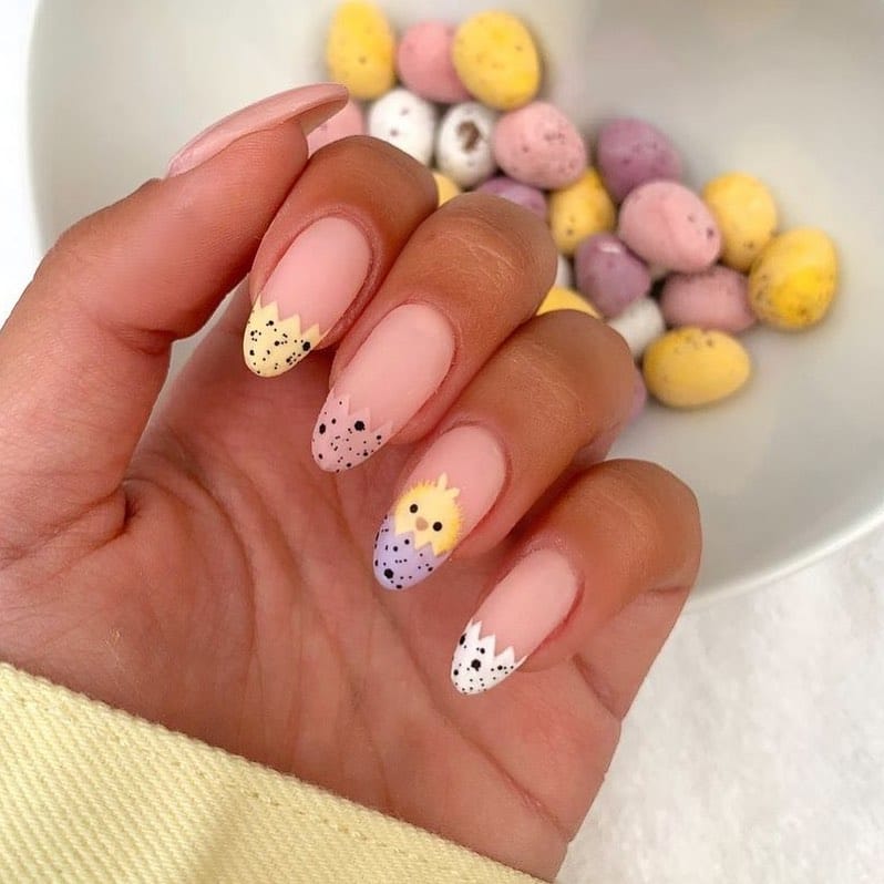 Hand with chick nail art and pale yellow sleeve next to chocolate eggs.