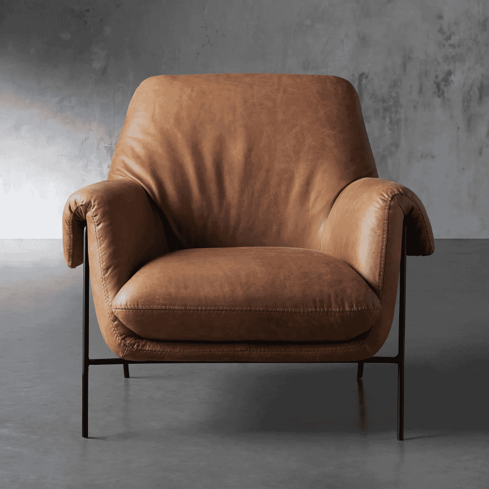 A brown leather armchair with metal legs against a gray concrete wall.