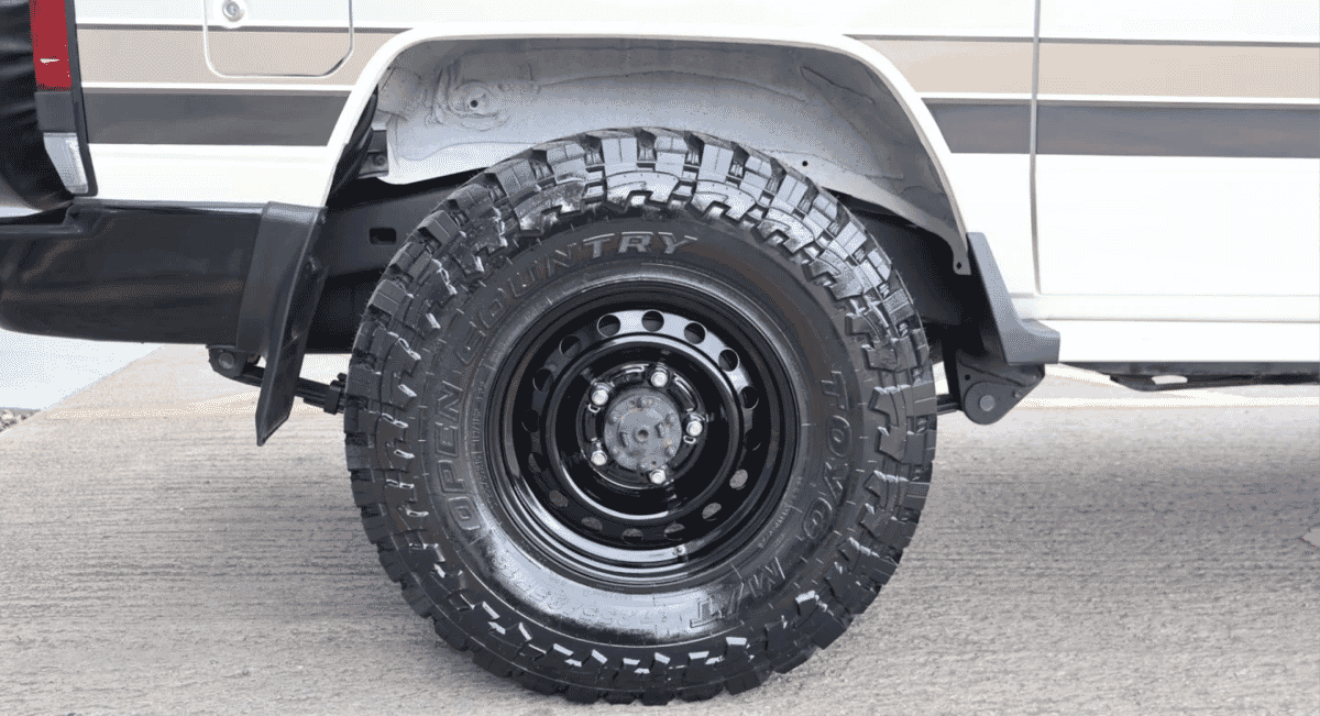 Close-up of a rugged all-terrain tire and black alloy wheel with a distinctive beige stripe.