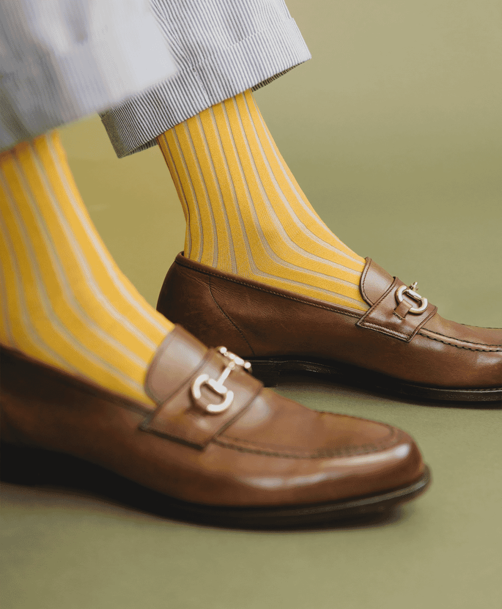 Man's feet in yellow striped socks and brown leather loafers with metal buckles.