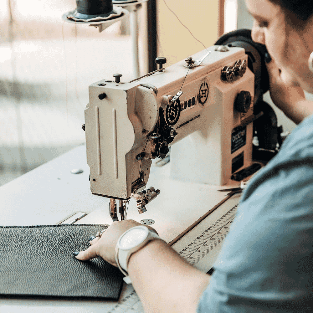 A person using an industrial sewing machine to stitch black textured leather.