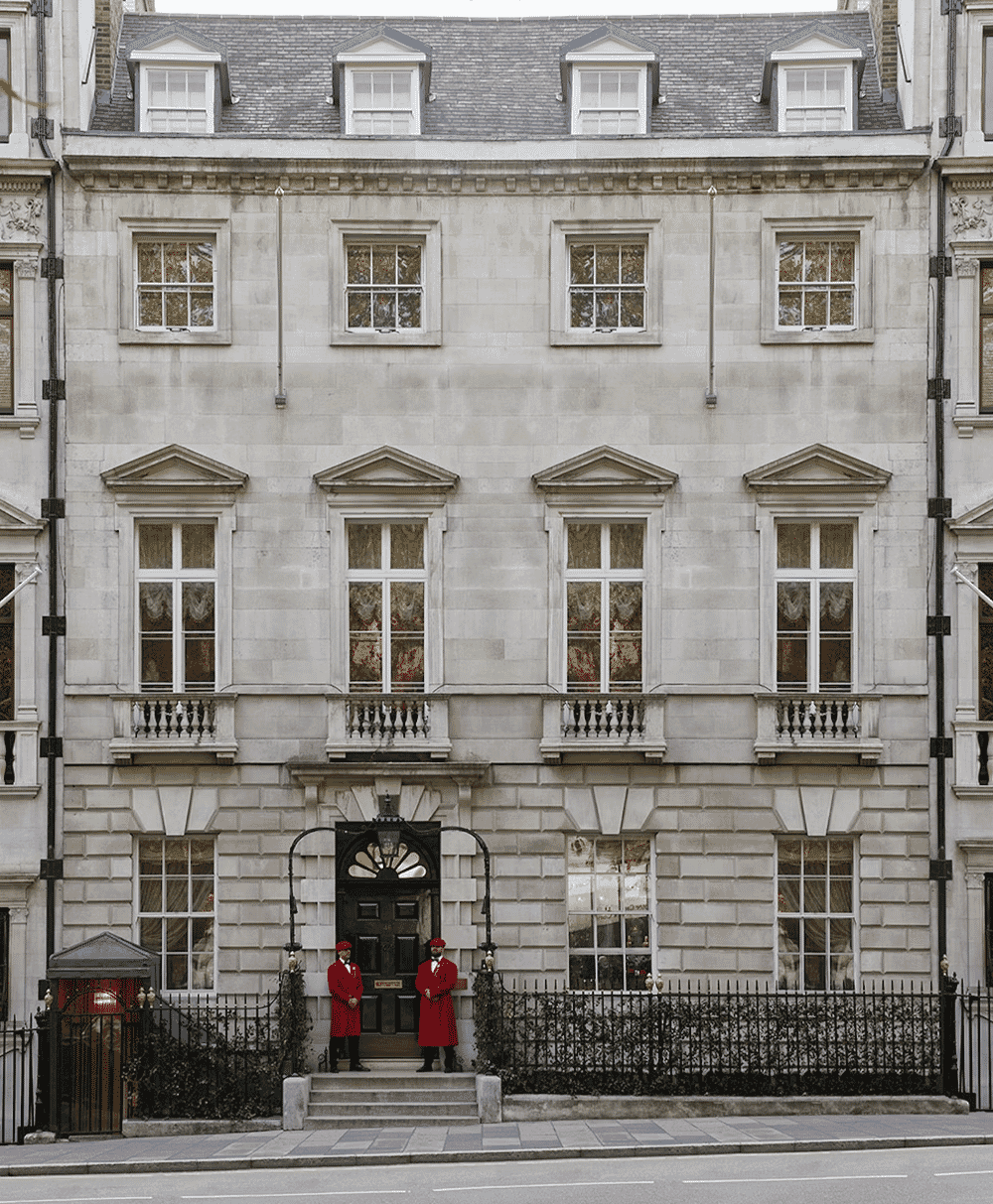 Two doormen in traditional red uniforms standing at a grand stone entrance.