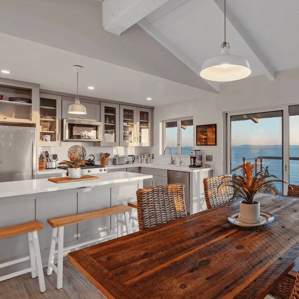 A bright modern coastal kitchen featuring white cabinetry and ocean views through large windows.