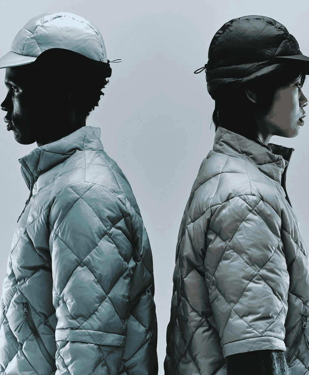 Two models in monochromatic quilted jackets and caps facing away from each other.
