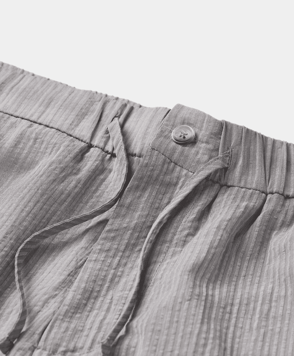 Close-up of light-colored, vertically striped trousers featuring a drawstring waistband and textured fabric.