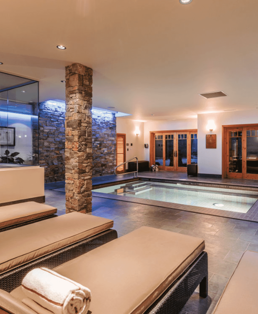 Indoor luxury spa with stone pillars and a swimming pool overlooking a mountain scene.