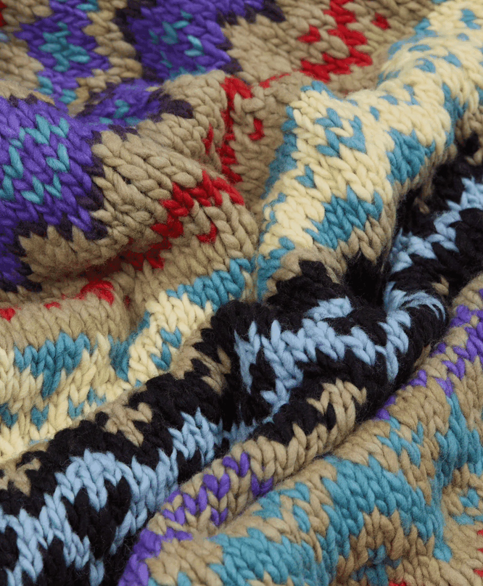 Extreme close-up of a chunky knit textile with purple, teal, and red geometric patterns.