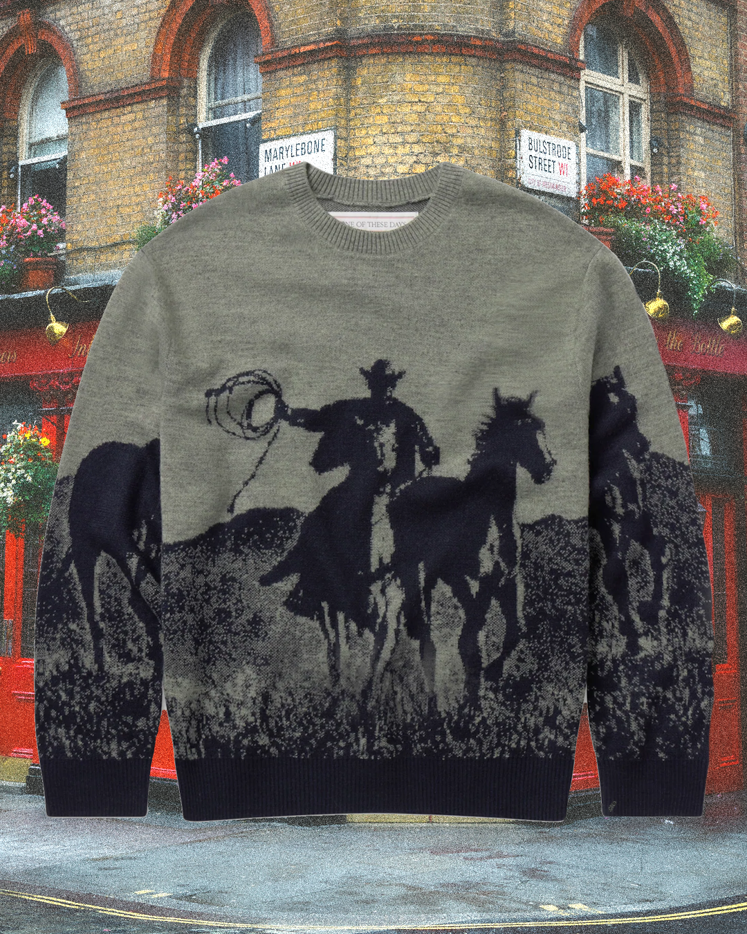 A grey knit sweater featuring a black silhouette of a cowboy on horseback against a brick building.