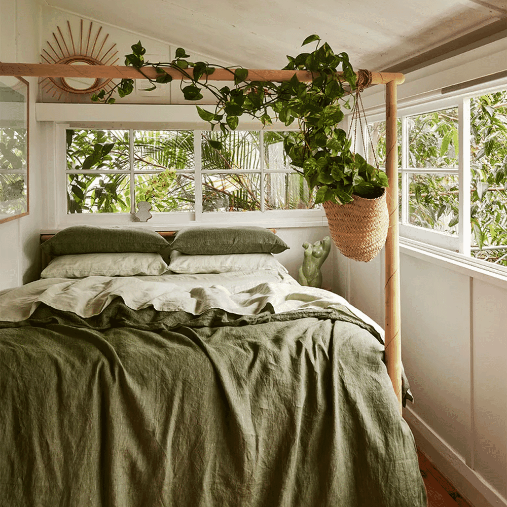 Bohemian-chic bedroom with olive green linen sheets, natural light, and hanging potted plants.
