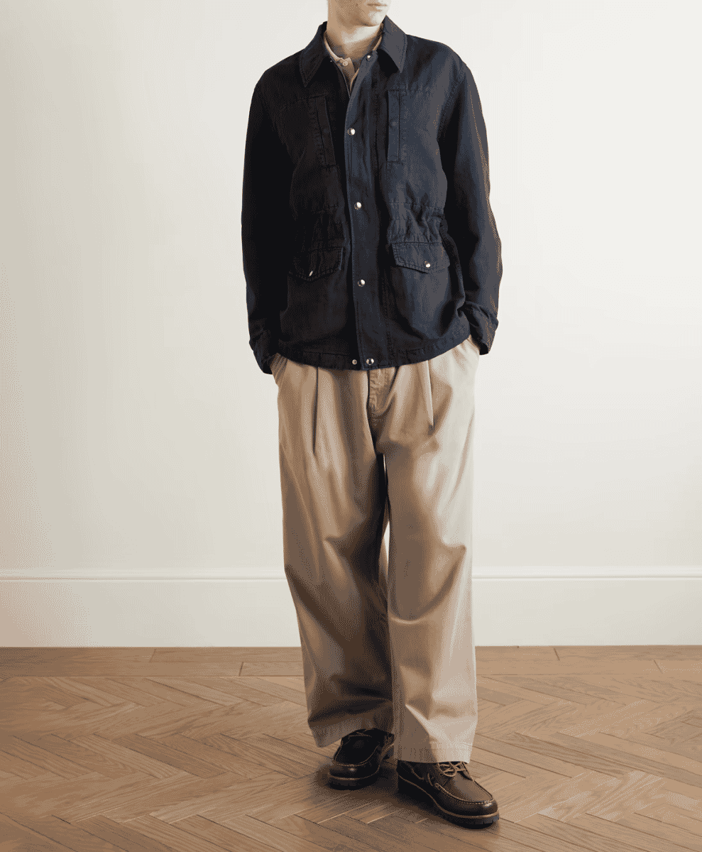 A man modeling a navy field jacket over a light shirt and beige pleated trousers.
