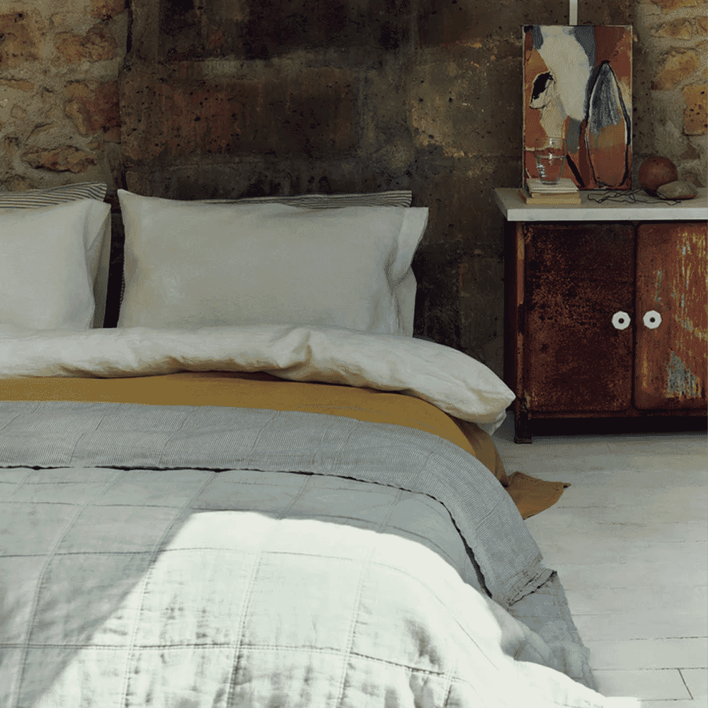 Layered neutral and mustard bedding in a rustic bedroom with a prominent stone wall.