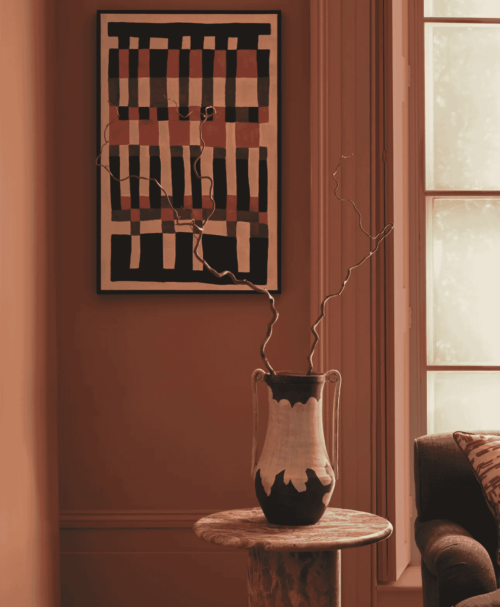 A geometric abstract painting displayed on a marble table with a ceramic vase in a warmly lit room.