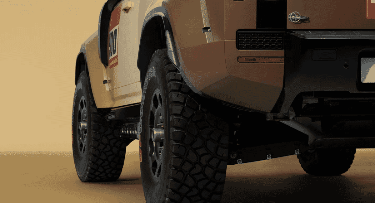 Close-up of rugged off-road tires and technical decals on a beige Land Rover Defender rally car.