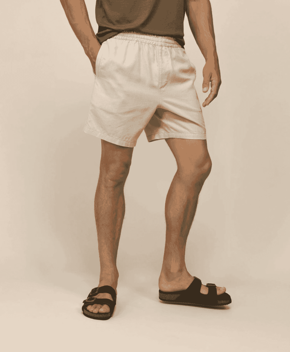 Full body studio shot of a man wearing white elastic-waist linen shorts and a brown t-shirt