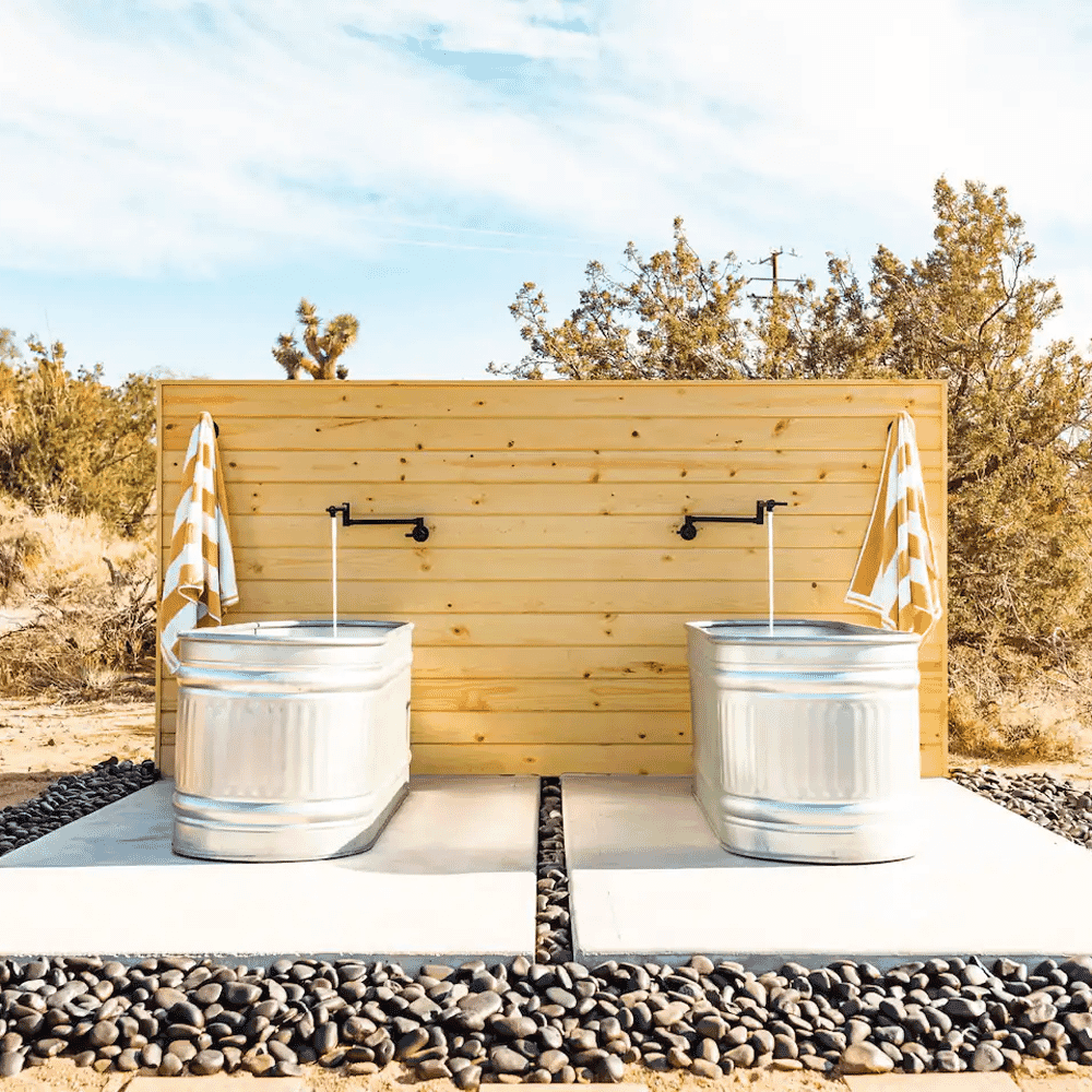 Outdoor rustic sink station with metal basins against a wooden wall in a desert setting.