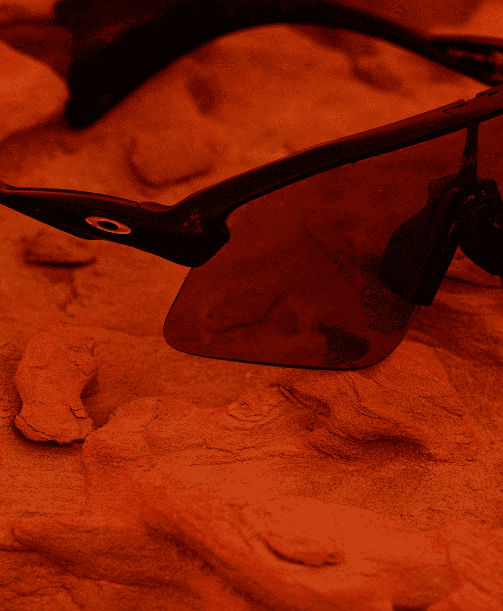 Black Oakley sunglasses resting on textured rocky terrain with a warm orange filter.