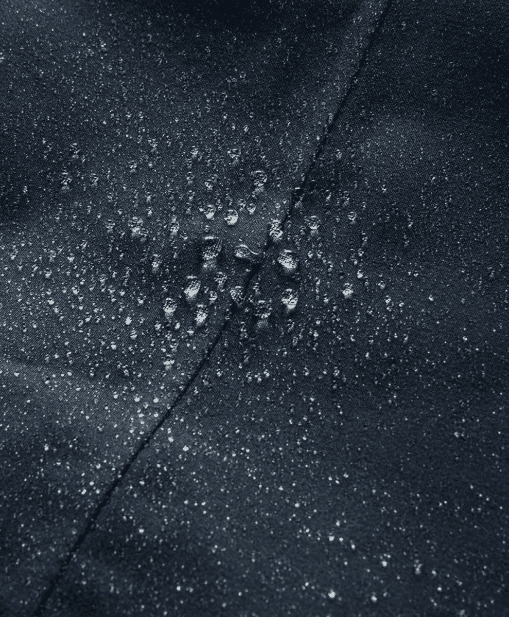 Extreme close-up of water droplets beading on dark waterproof fabric.
