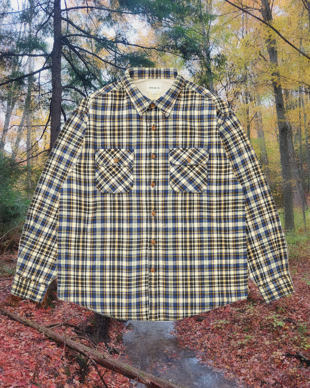 Blue and yellow plaid flannel shirt with chest pockets against a forest background.