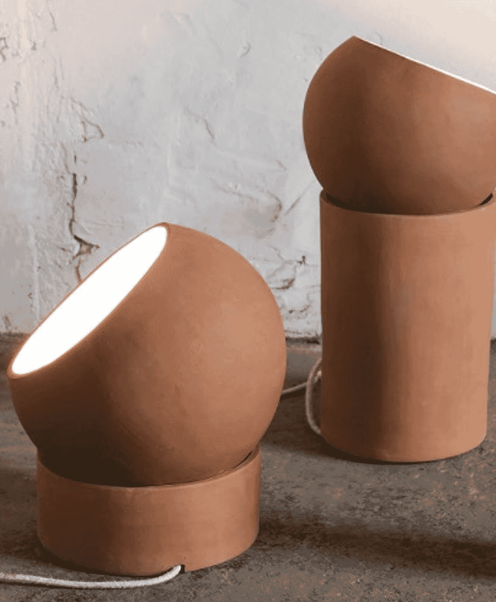 Two terracotta-colored ceramic table lamps with minimalist designs on a textured surface against a white wall.
