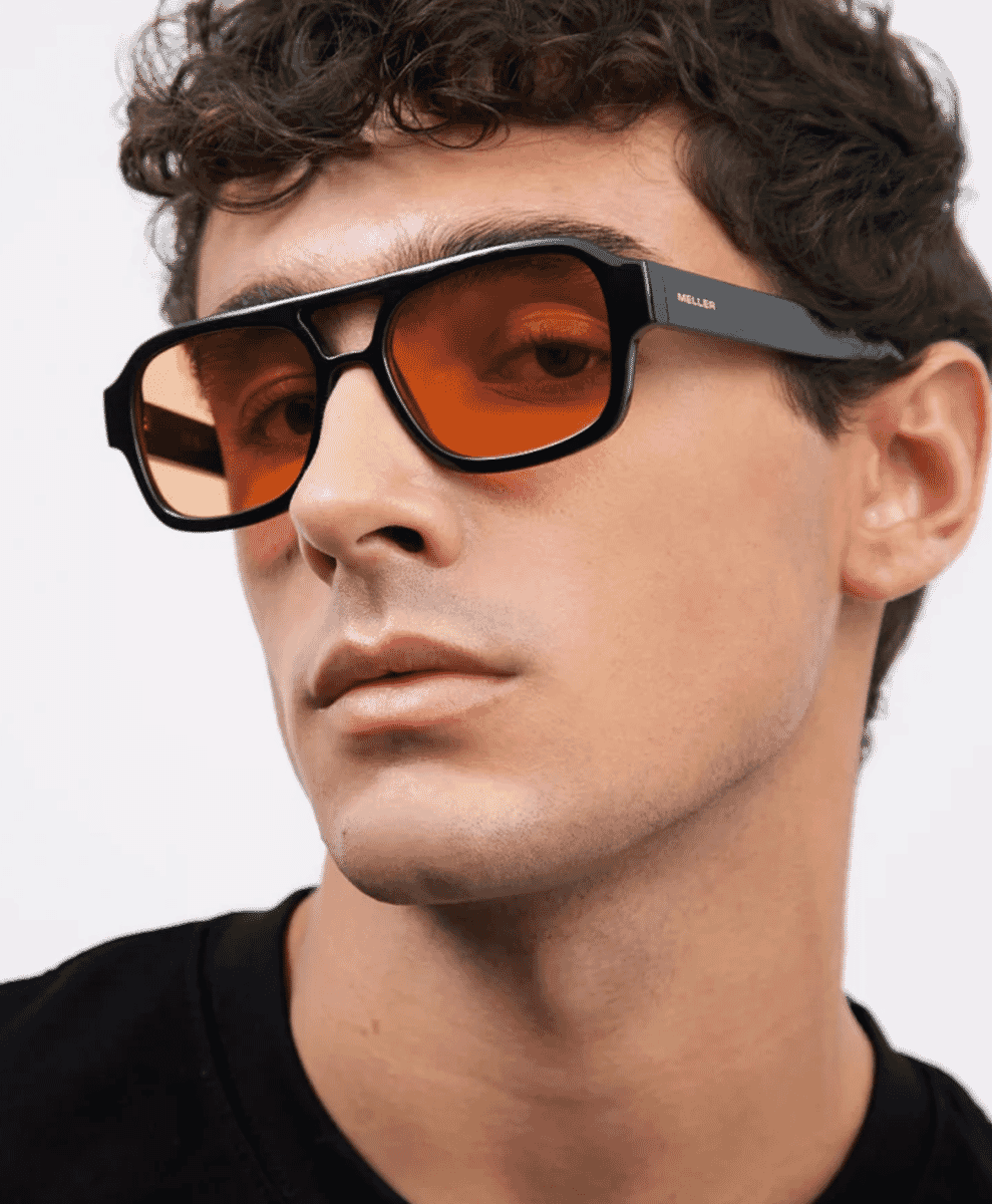 Close-up of a man wearing bold black-framed sunglasses with orange lenses.