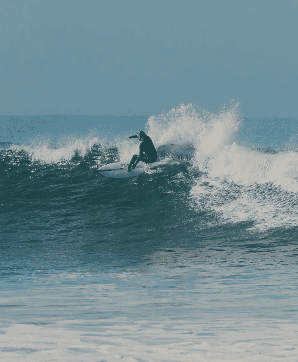 A surfer in a black wetsuit catching a wave on a white surfboard.
